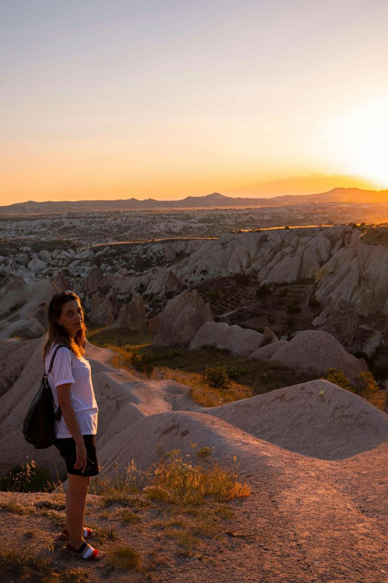 A woman explores the stunning rock formations of Cappadocia's Red Valley at sunset, capturing adventure and natural beauty.