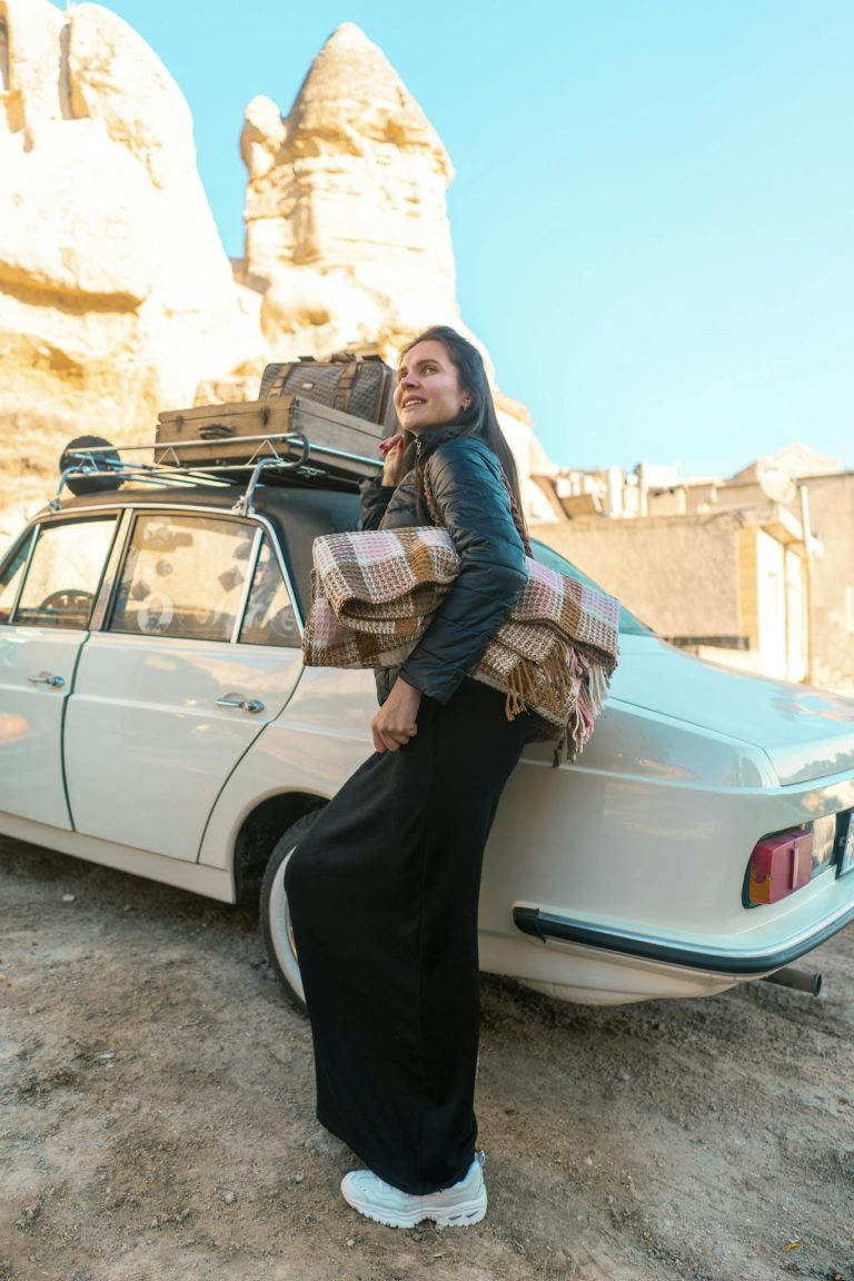 Smiling woman leaning on a vintage car with rocky formations in Cappadocia, Turkey.